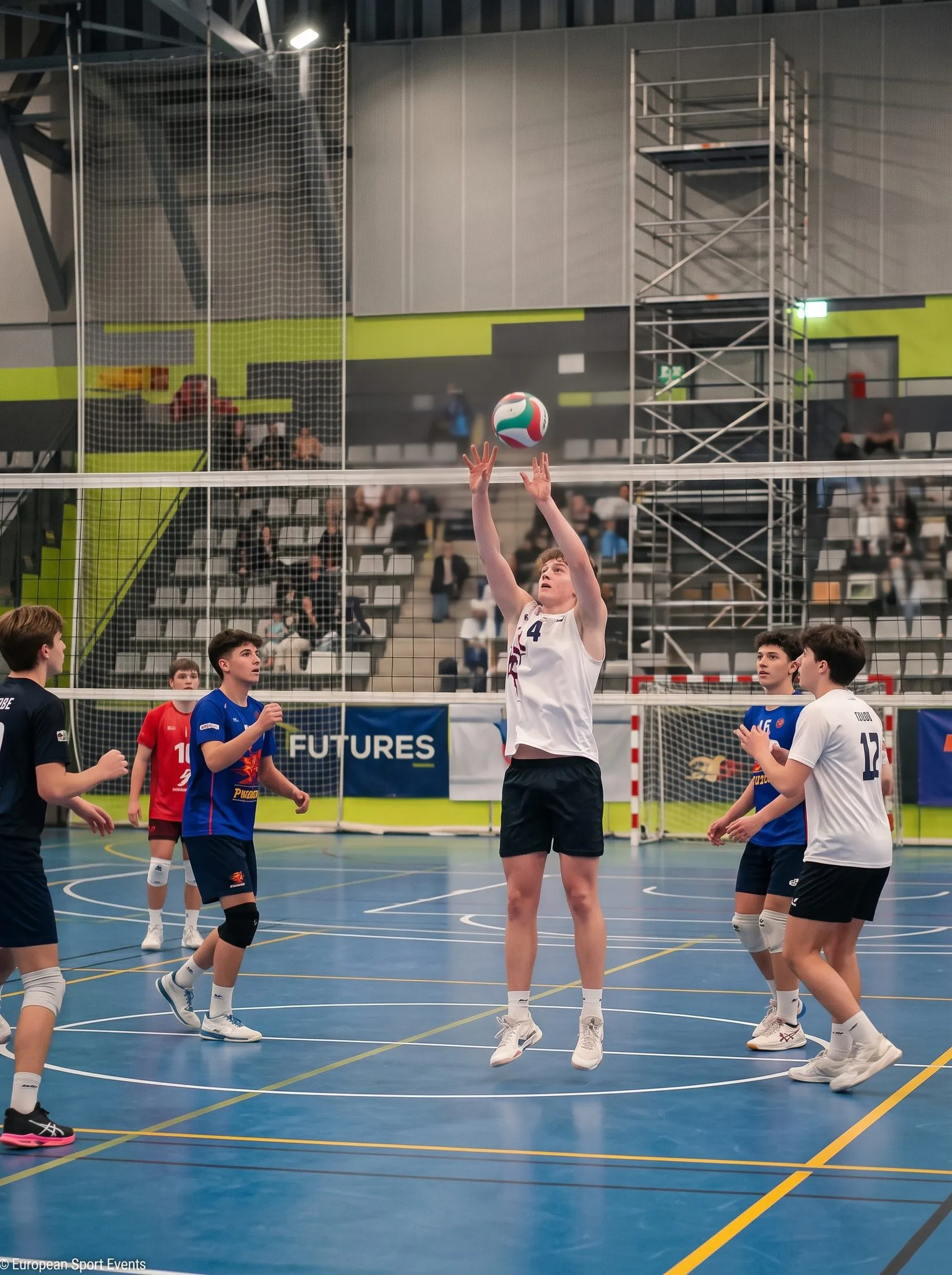 Un jugador de voleibol colocando el balón junto a la red en un pabellón durante un partido amistoso